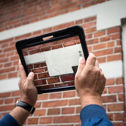 Met een tablet wordt een foto gemaakt van een scheur in een buitenmuur. 