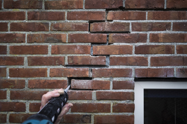 Een scheur in een buitenmuur wordt door een stukadoor hersteld.
