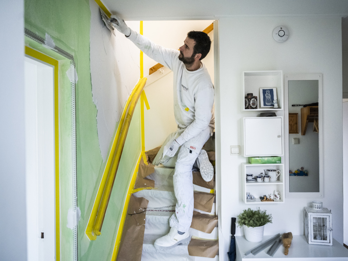 Persoon stukt een wand naast de trap naar de bovenverdieping in een huis.