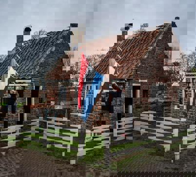 Beheerder van het kleinste huis van Rottum hangt de vlag uit, op de achtergrond een borstbeeld van schrijver Jan Boer.