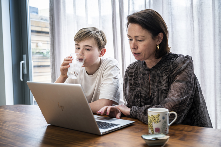 Moeder en zoontje zitten samen achter de laptop aan de keukentafel.