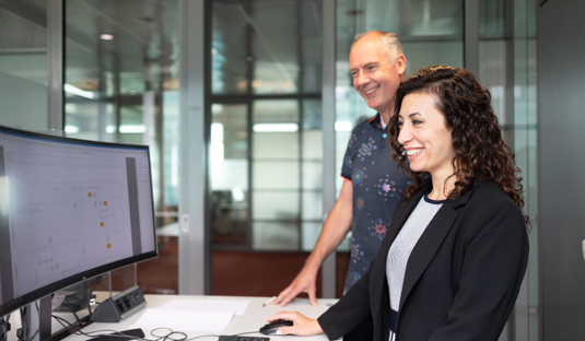 Foto van twee collega's die achter een computer staan.