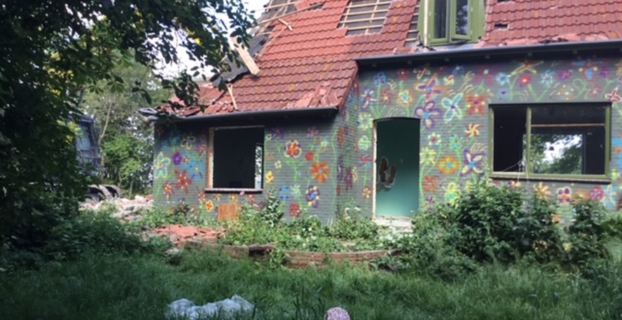 In een verwilderde tuin staat een vervallen, leegstaand huis dat is beschilderd met bloemen in allerlei kleuren