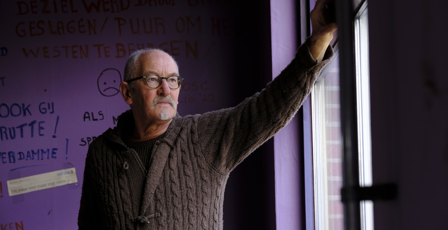Koos Cleveringa staat in zijn huis voor een muur met teksten over de gaswinning en kijkt uit het raam