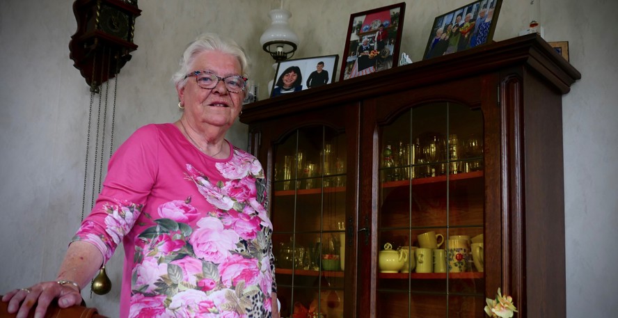Jopie van der Wal-Balkema staat in haar woonkamer voor een kast met mooie spulletjes en foto's