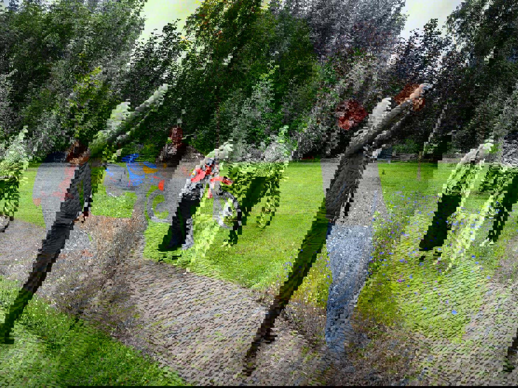 Drie personen en een hond staan in een grote tuin, waarbij een persoon zijn camera richt om een foto te maken.