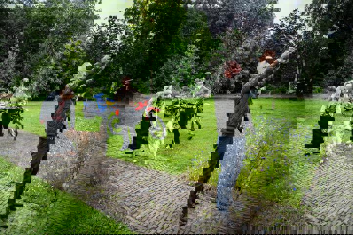 Drie personen en een hond staan in een grote tuin, waarbij een persoon zijn camera richt om een foto te maken.