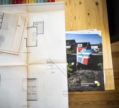 Op tafel liggen papieren waarop een bouwtekening van een woning zichtbaar is met erachter de map met documenten van Instituut Mijnbouwschade Groningen.