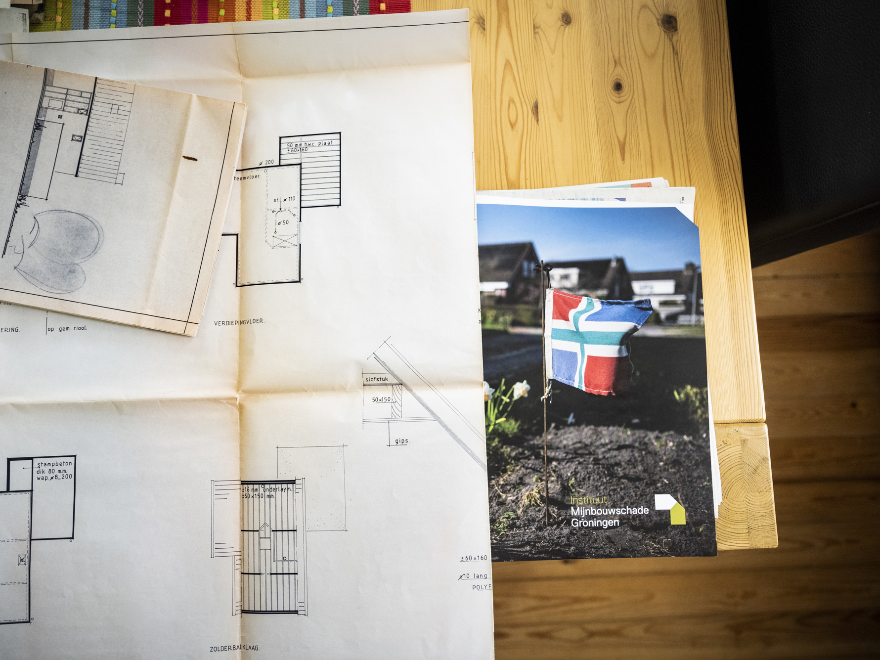 Op tafel liggen papieren waarop een bouwtekening van een woning zichtbaar is met erachter de map met documenten van Instituut Mijnbouwschade Groningen.