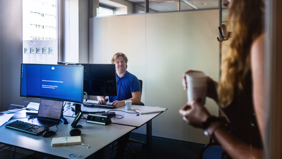 Niels zit aan een bureau en ziet een collega zijn kantoorruimte binnenkomen.