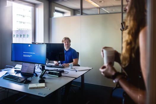 Niels zit aan een bureau en ziet een collega zijn kantoorruimte binnenkomen.
