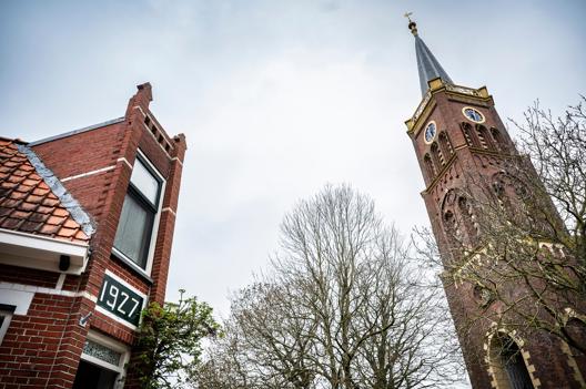 Links een hoekwoning met markante gevel, rechts de kerktoren.