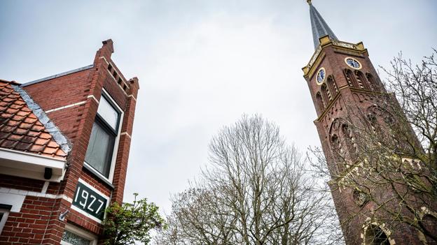 Links een hoekwoning met markante gevel, rechts de kerktoren.