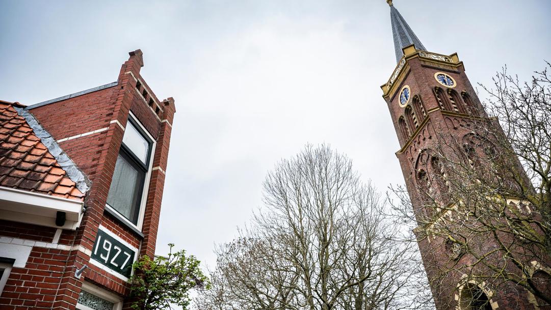 Links een hoekwoning met markante gevel, rechts de kerktoren.