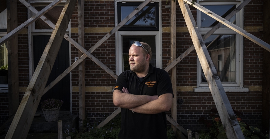 Erwin van der Laan staat met gekruiste armen voor zijn huis dat door houten stutten overeind wordt gehouden