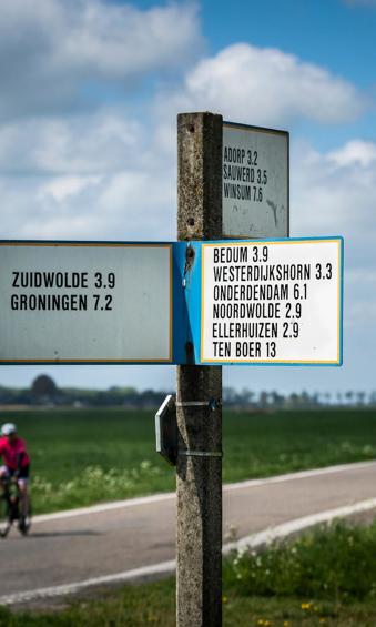 Wegwijzer met namen van dorpen uit het hogeland met op de achtergrond twee fietsers.