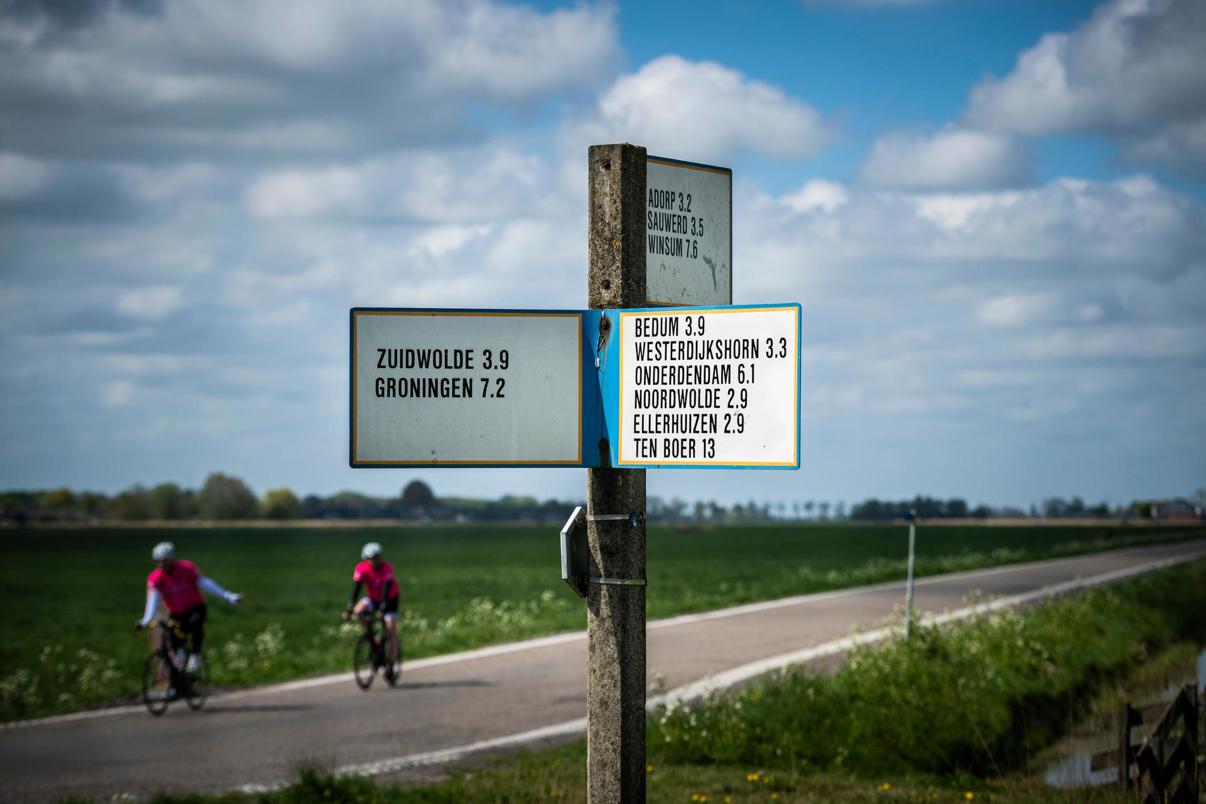 Wegwijzer met namen van dorpen uit het hogeland met op de achtergrond twee fietsers.