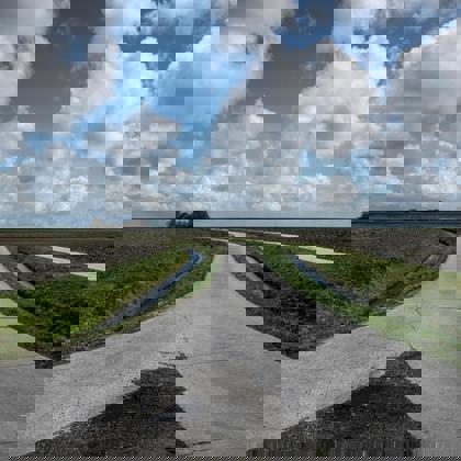 Twee landwegen komen samen tussen weilanden in het Groninger landschap.