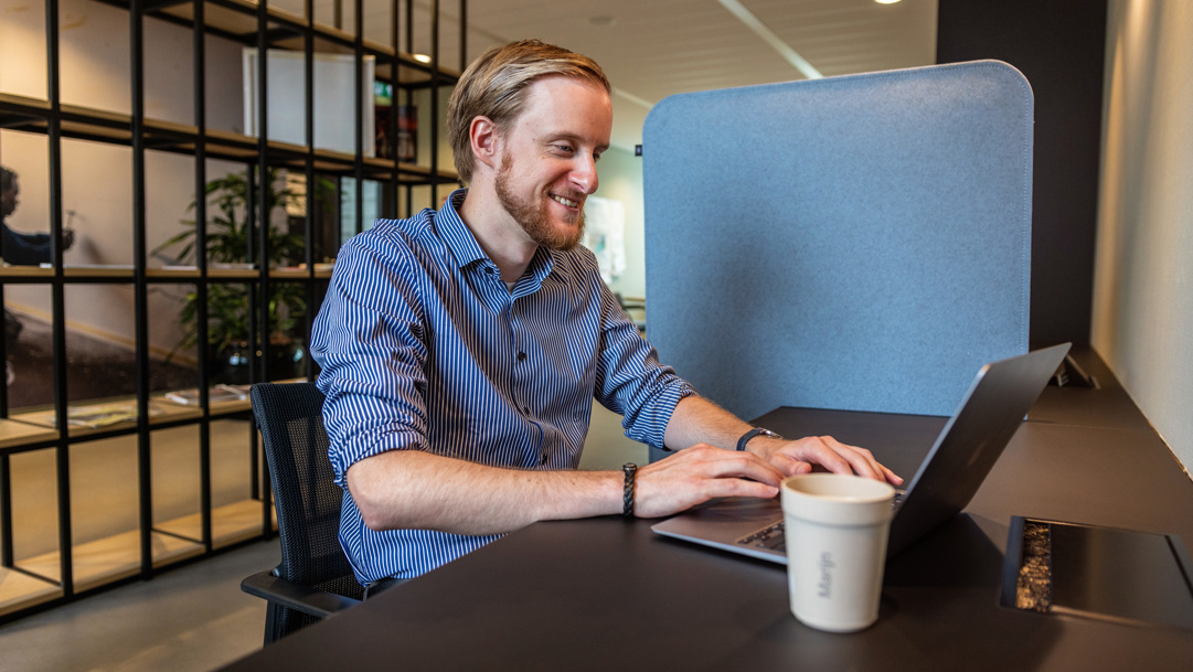 Marijn zit glimlachend achter zijn laptop aan het werk.