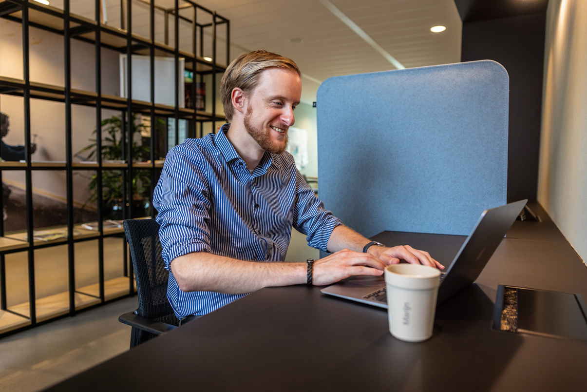 Marijn zit glimlachend achter zijn laptop aan het werk.