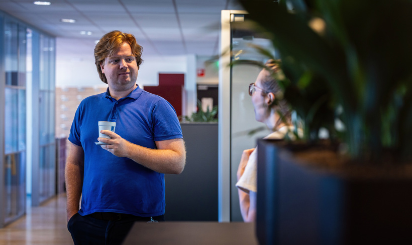 Niels praat met een collega terwijl hij een kopje koffie vasthoudt.