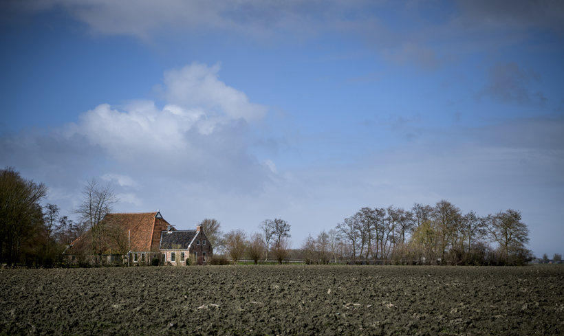 Omgeploegd veld met op de achtergrond een agrarisch bedrijf.